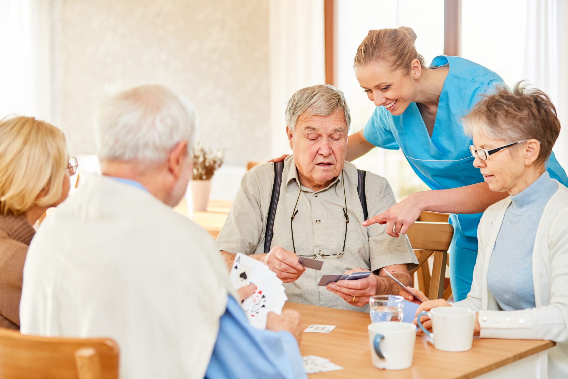 Elderly individuals playing cards with a caregiver assisting in a warm, friendly setting.